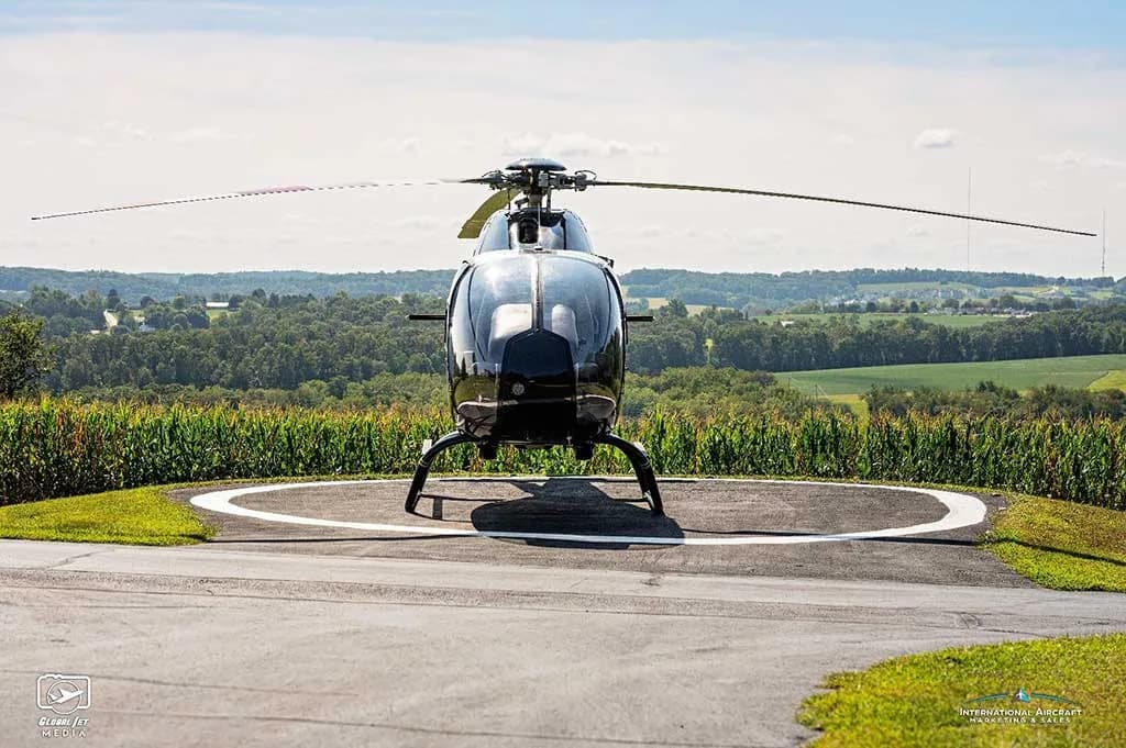 Front view of a black Eurocopter AS350 helicopter (N123PE) on a helipad overlooking a rural landscape.