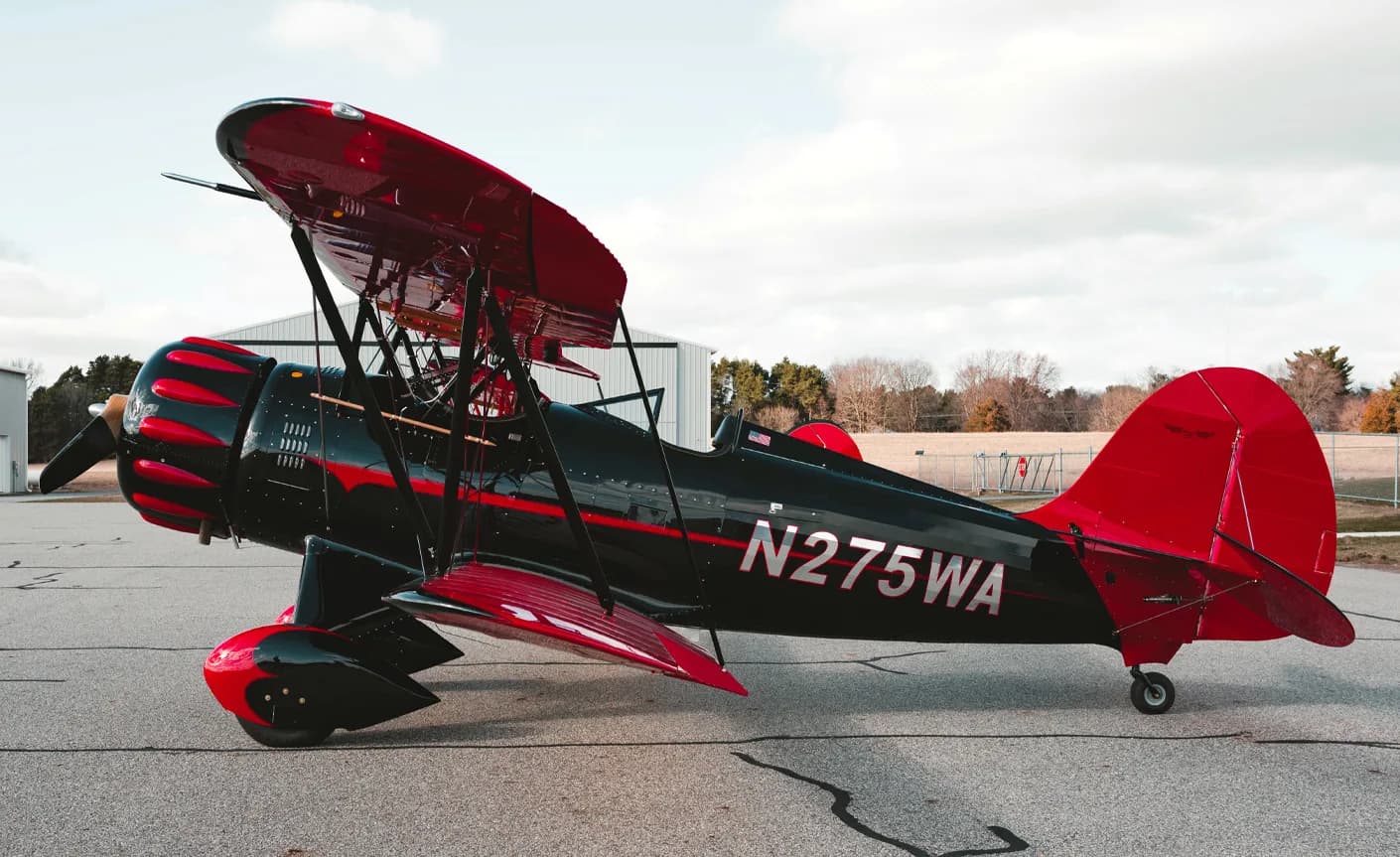 A black and red biplane with tail number N275WA is parked on the tarmac.
