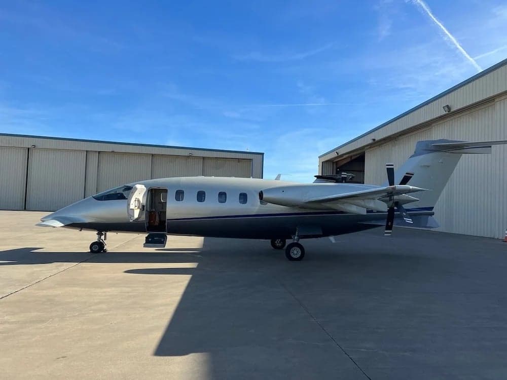 A Piaggio Avanti EVO aircraft is parked outside a hangar on a sunny day.