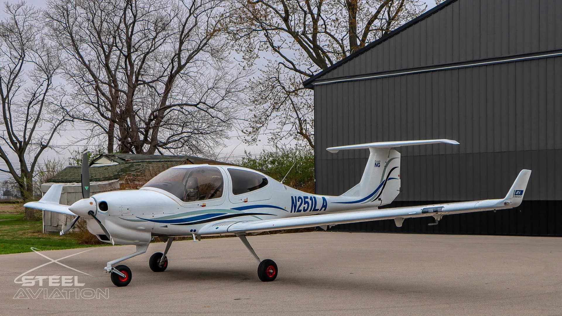 Side view of a white Diamond DA40 NG aircraft, N251LA, with blue and grey stripes parked on an apron.