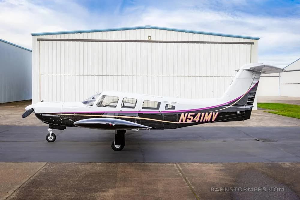 A white and black single-engine aircraft with purple stripes (N541MV) parked on an asphalt apron under a blue sky.