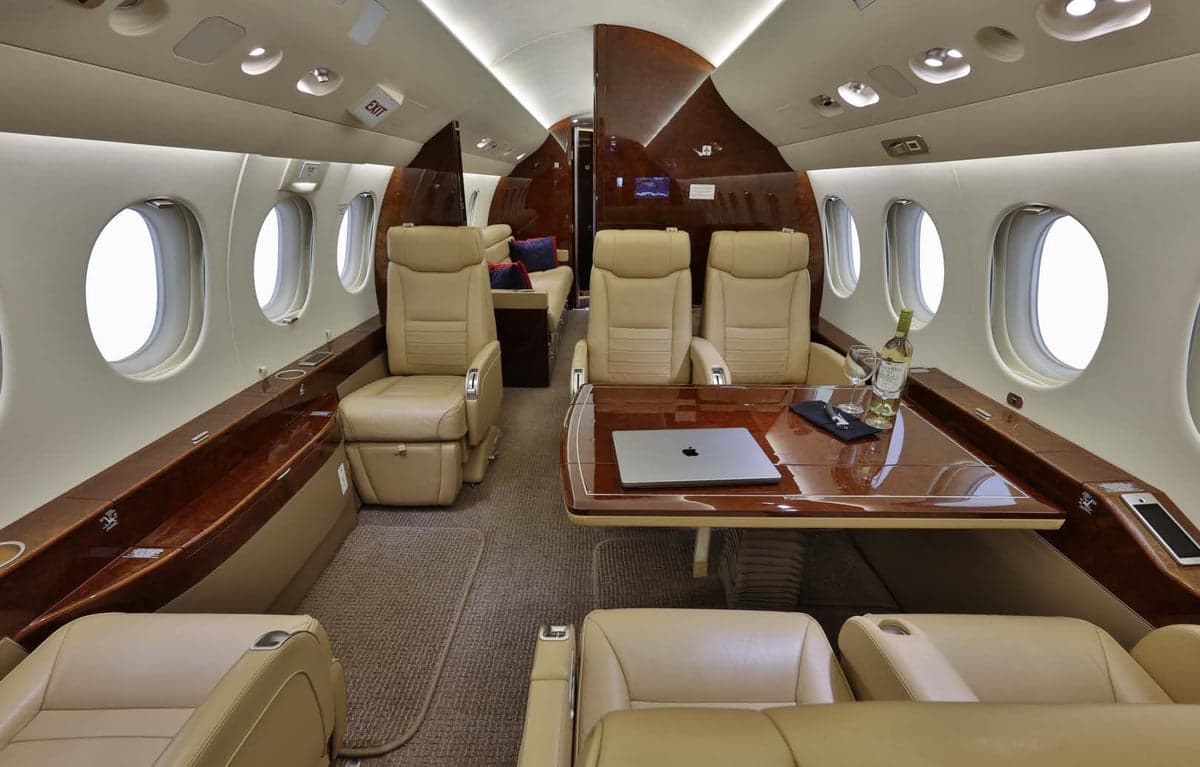 The aircraft's interior features tan leather seats and a table with a laptop and wine glasses.
