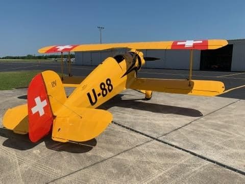 A yellow biplane with Swiss markings parked on the tarmac.
