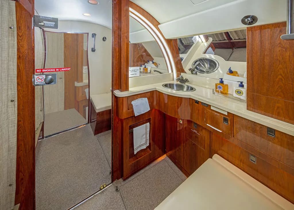 The lavatory area of a private jet features a sink, mirror, and rich wood cabinetry.