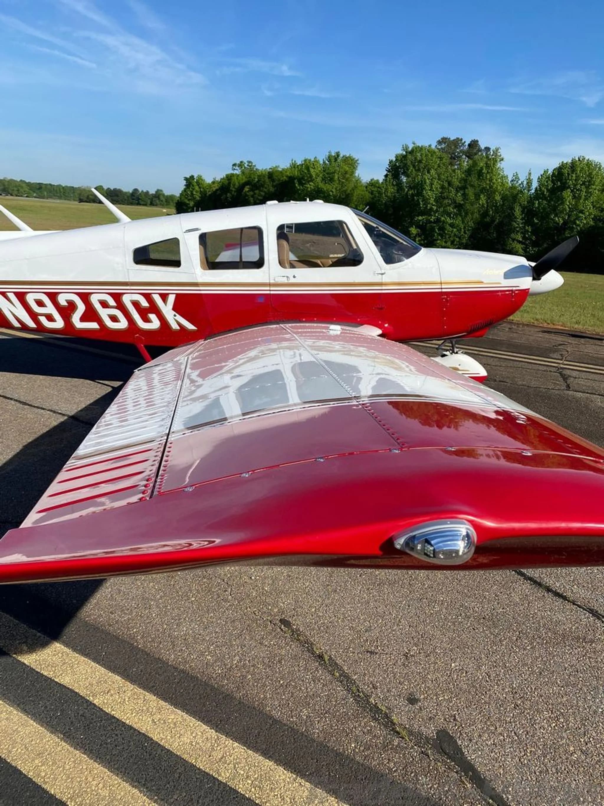 A close-up view of the right wing and fuselage of a white and red Piper Arrow II (N926CK) on the tarmac.