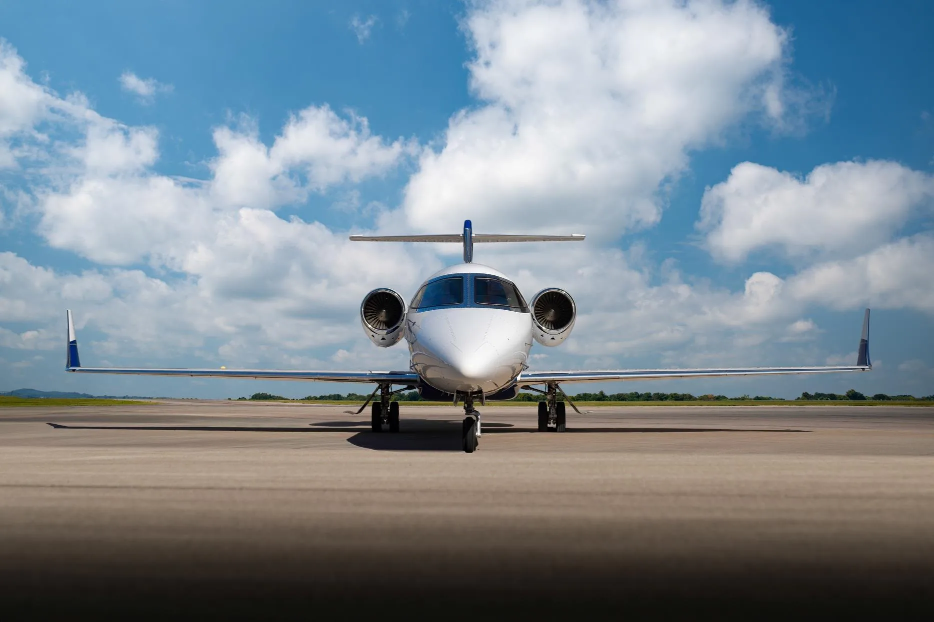 Head-on view of a white and blue Learjet 75 business jet, registration N214TG, parked on a tarmac.