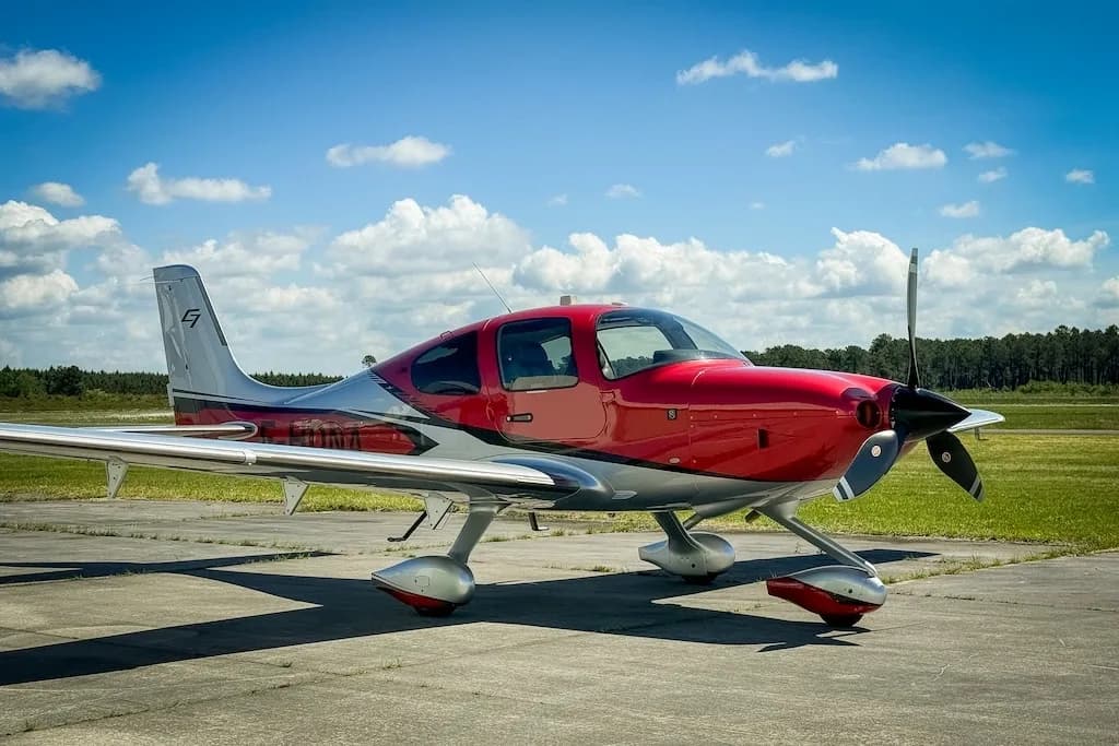 A red and silver Cirrus SR22 GTS aircraft parked on a tarmac under a blue sky.