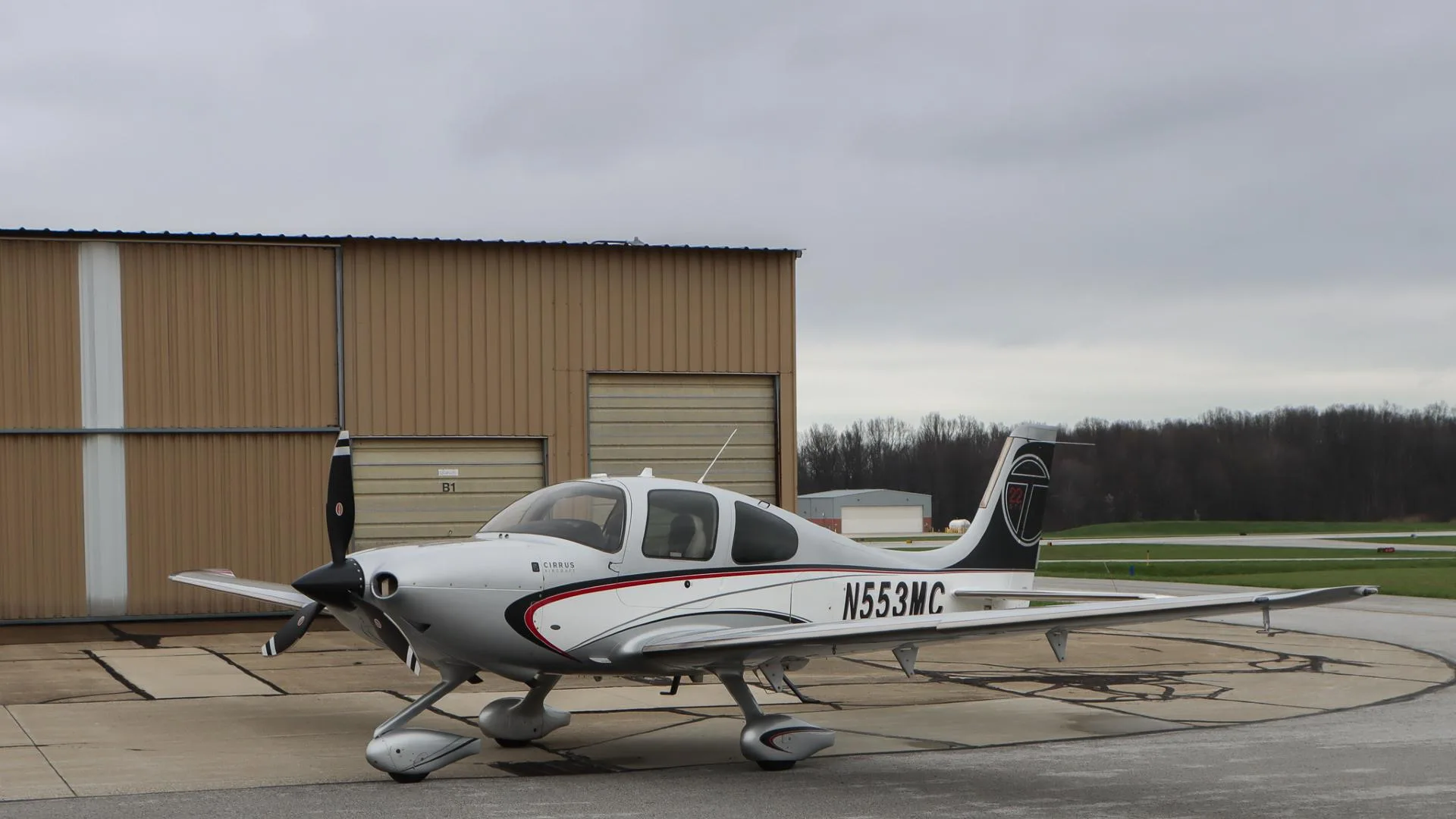 A left side view of the Cirrus SR22 N553MC, showing the full aircraft and a hangar in the background.