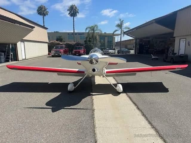 A white and red single-engine aircraft, possibly an experimental or aerobatic type, viewed from the front, parked on an asphalt apron.