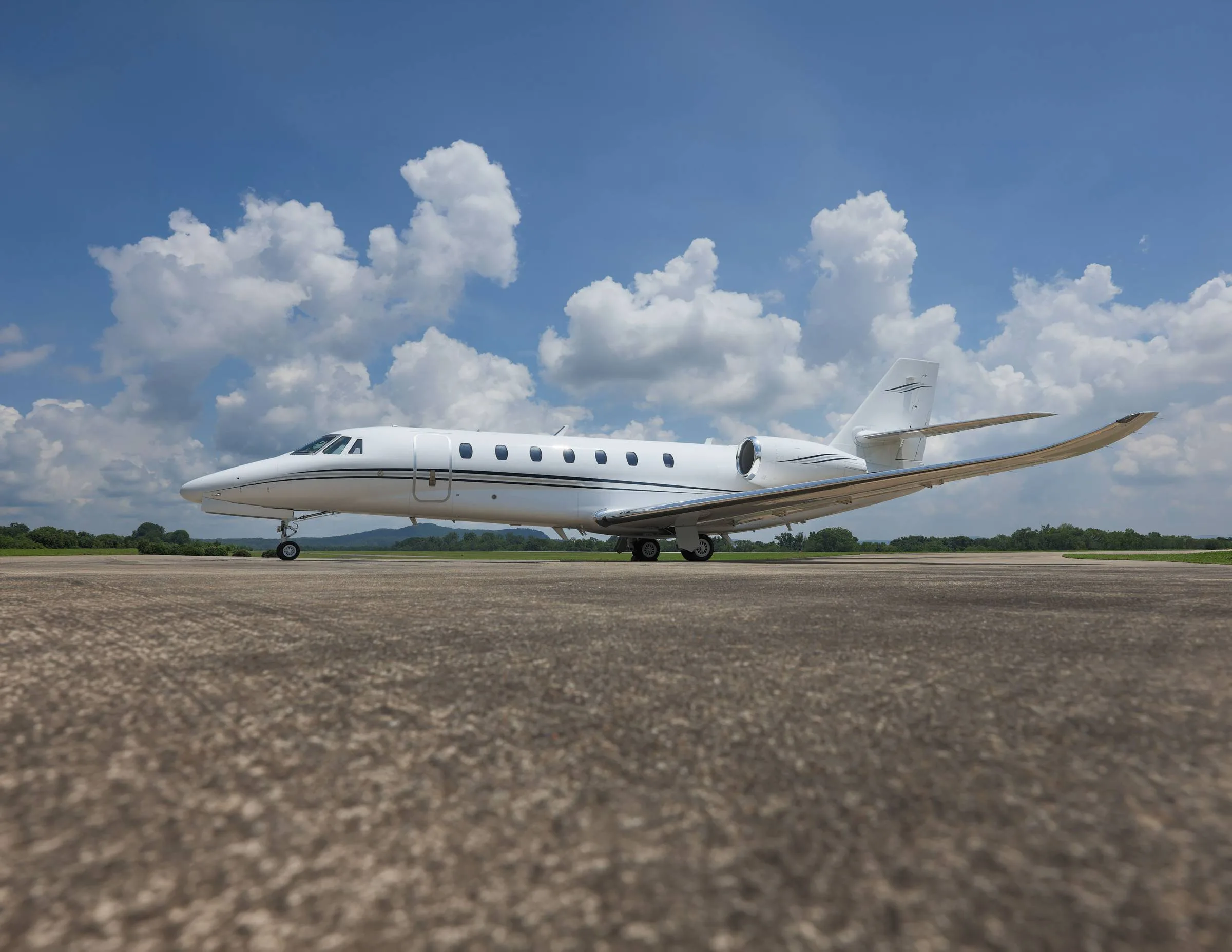 A white business jet with black stripes on an airfield under a blue sky with clouds.