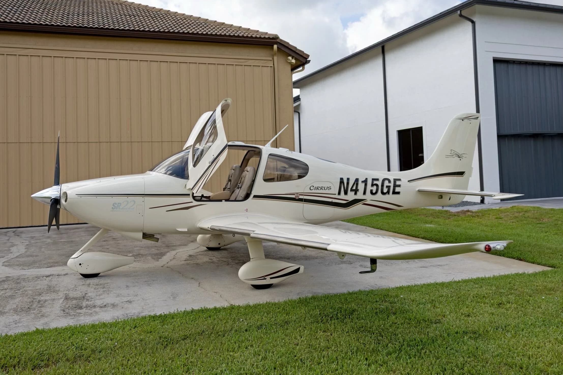 A white Cirrus SR22 aircraft with black and maroon stripes, registration N415GE, parked with its gull-wing doors open.