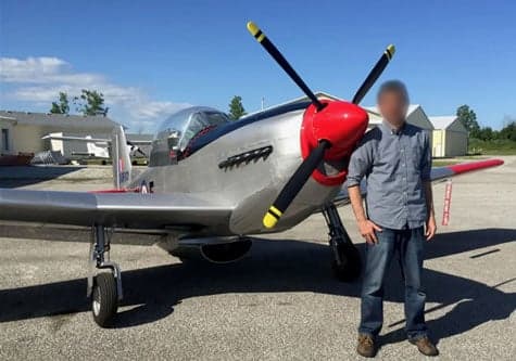 A silver and red aircraft is parked on the tarmac with a person standing next to it.