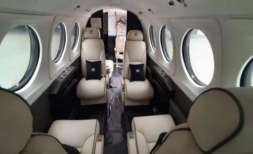 The interior cabin of an aircraft features light beige leather seats with black pillows and small round windows.