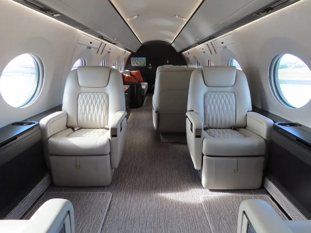 Aircraft cabin with leather seats and round windows.