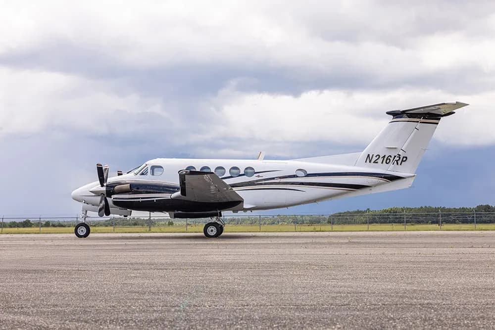 A King Air aircraft with registration N216RP is parked on the tarmac under a cloudy sky.