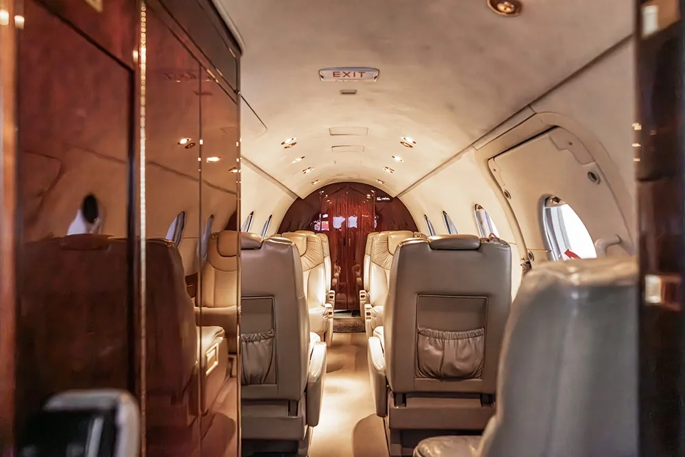 View down the aisle of a private jet cabin with light-colored leather seats and a visible "EXIT" sign.