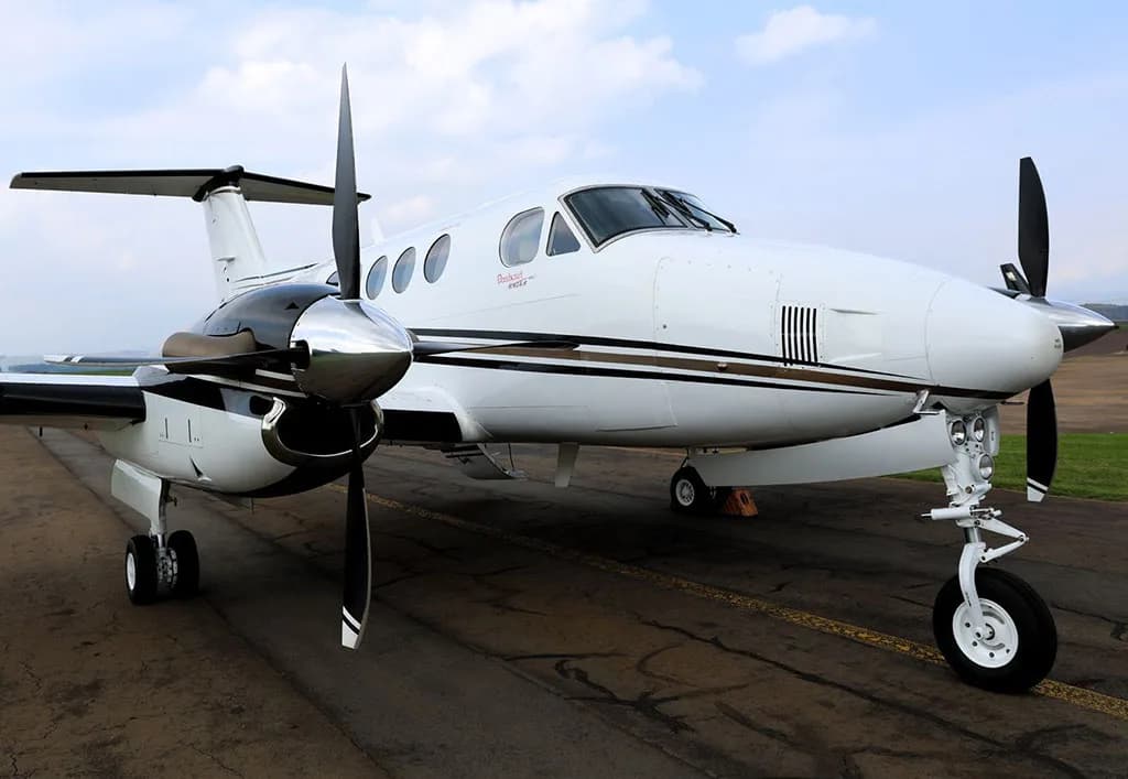 A front view of a white and black Beechcraft King Air 250 turboprop aircraft parked on an asphalt runway.
