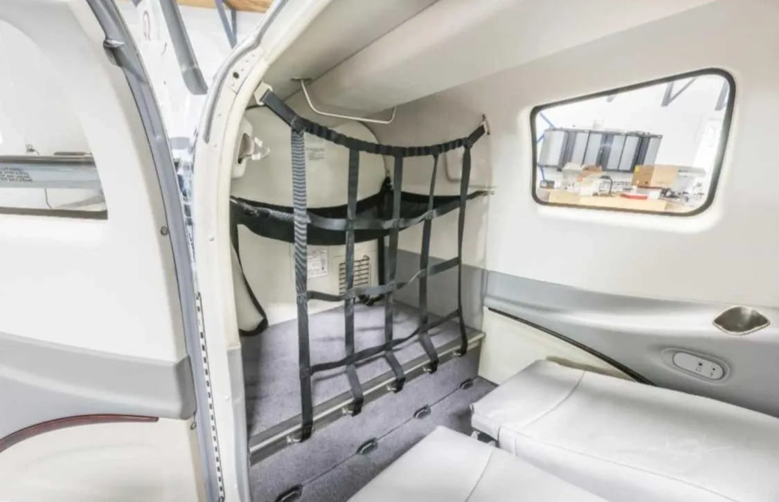The rear interior cabin of a small aircraft showing a cargo net and folded seats.