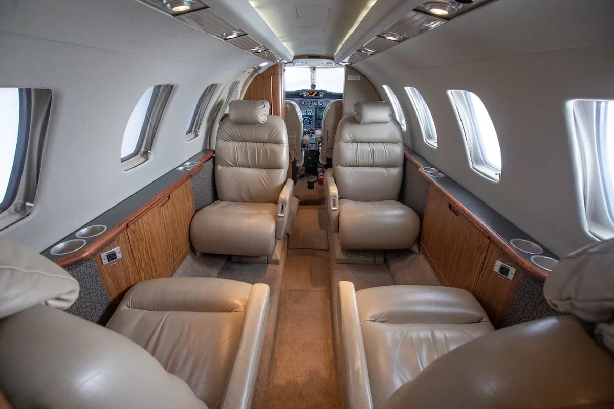 Private jet cabin with beige leather seats and two fold-out tables extended between them.