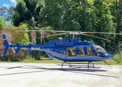 A blue Bell 407 helicopter is parked on the ground.