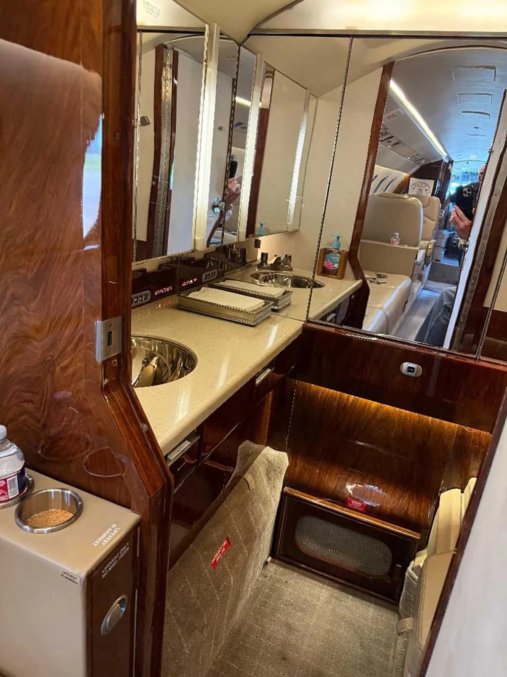 A view of the aircraft's galley or lavatory area with two sinks, mirrors, and polished wood cabinetry.