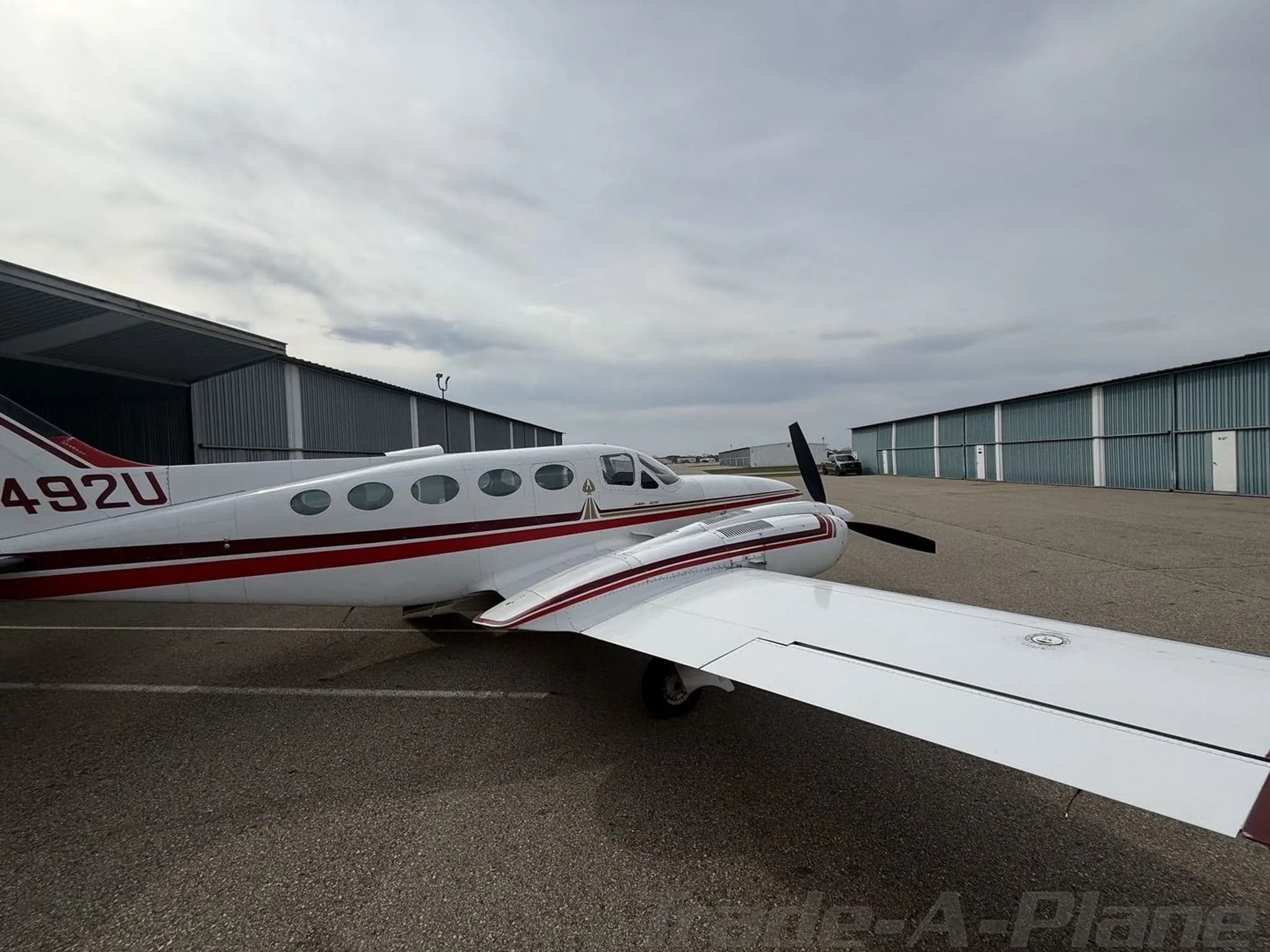 A side view of a white and red twin-engine Cessna 414 Chancellor aircraft, registration N4492U, parked on an asphalt ramp next to hangars.