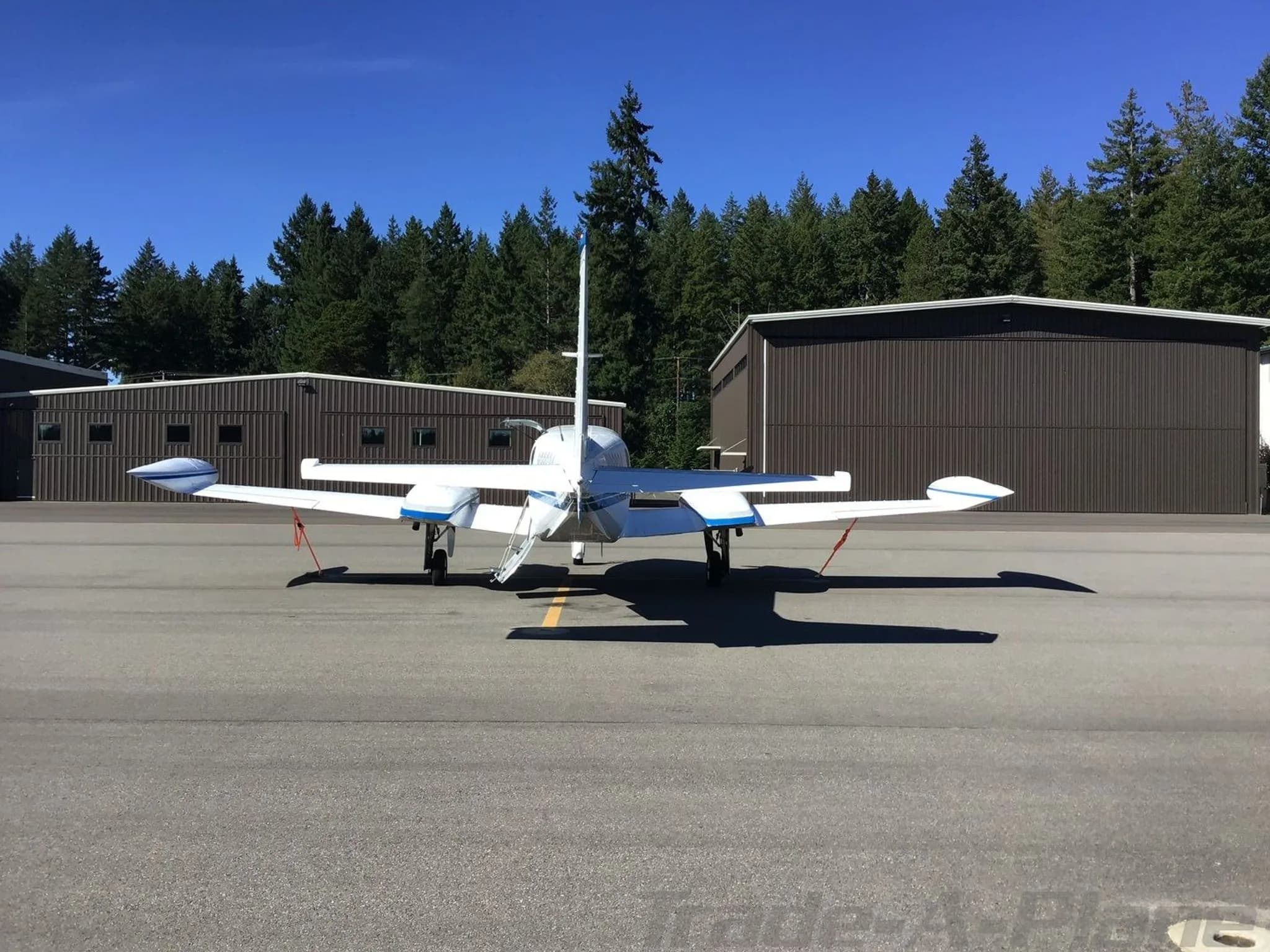 A rear view of the white and blue twin-engine Cessna 340 aircraft, N98624, parked on an airfield in front of hangars.