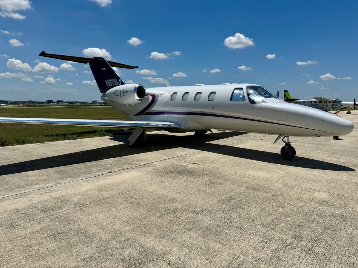 A white and purple Cessna Citation CJ1+ aircraft with registration N878J on the tarmac.