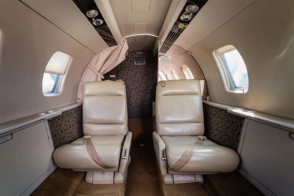 The interior cabin of a private jet, featuring two beige leather seats facing the rear.