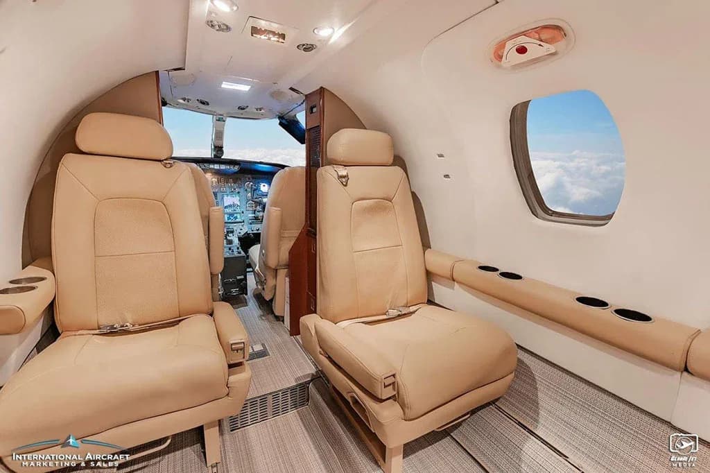A view from the rear cabin looking forward into the cockpit of a business jet with beige leather seats.