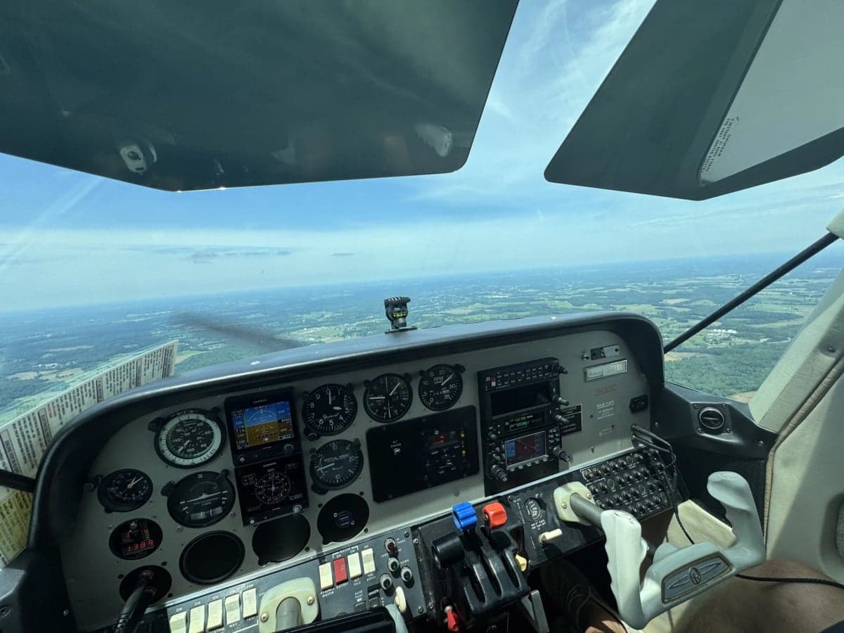 A wide view of the aircraft cockpit, showing the instrument panel and a scenic landscape from above.