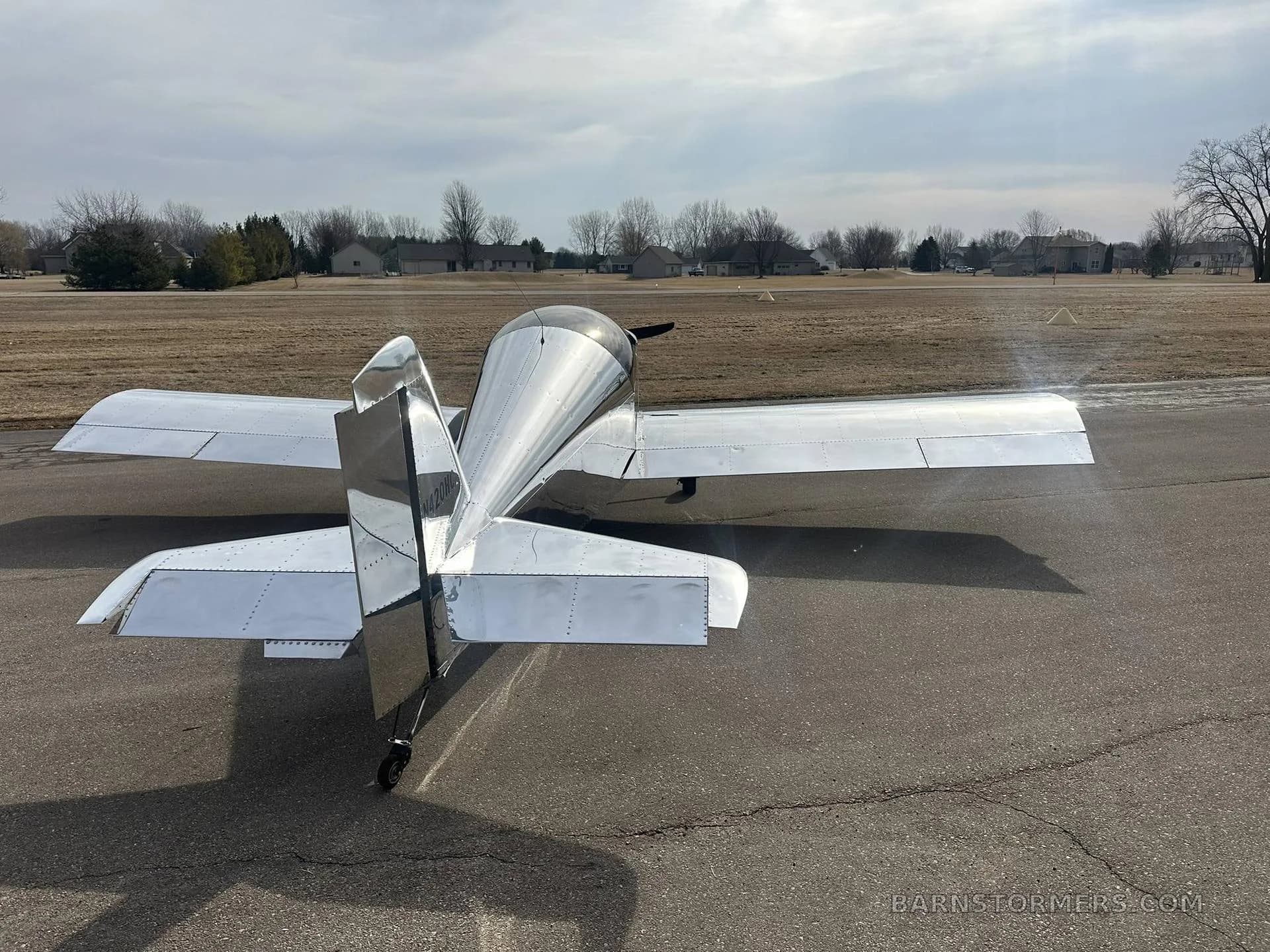 Rear view of a shiny silver experimental aircraft with a black tail, parked on an asphalt surface.