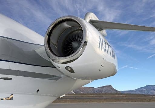 A Challenger 300 aircraft on the tarmac with mountains in the background.