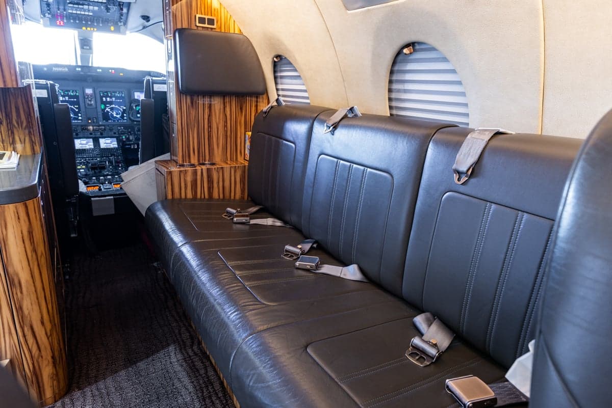 A leather bench seat is shown inside the aircraft cabin, with a view of the cockpit.