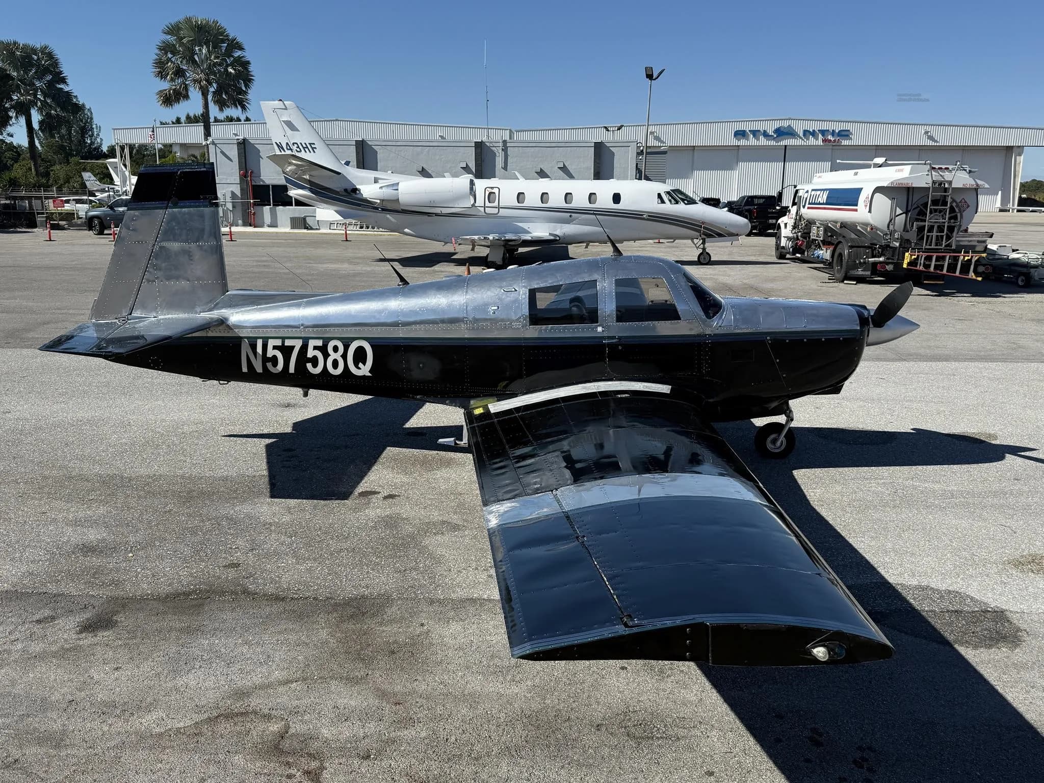 A black and silver Mooney M20 aircraft, N5758Q, parked on an asphalt tarmac next to a white business jet.