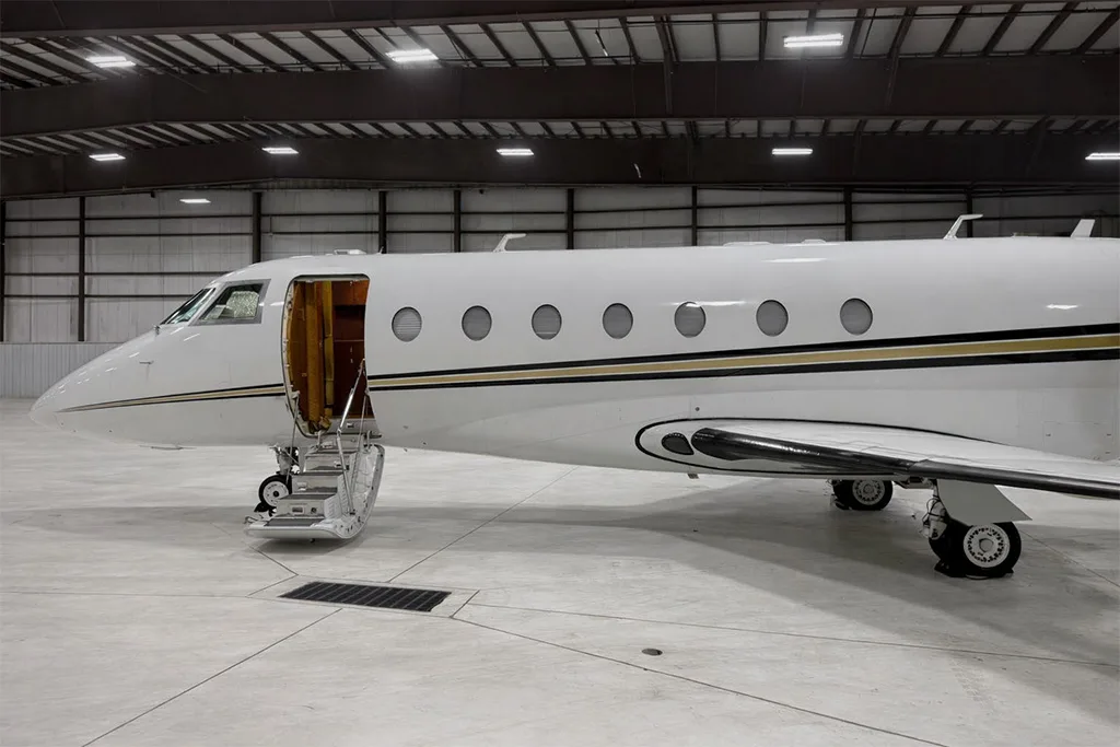 The front left side of a white Gulfstream business jet with its main entry door open and stairs extended, parked in a hangar.