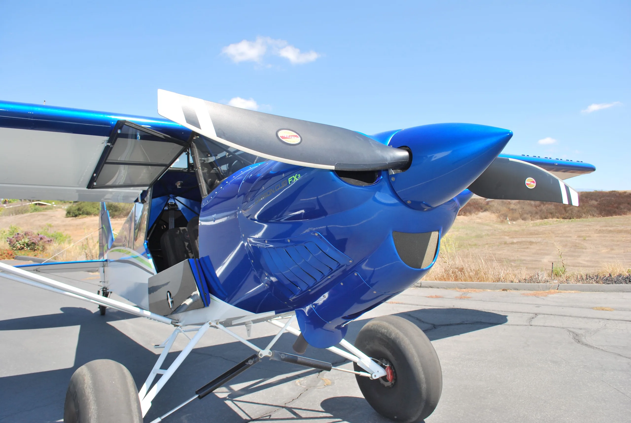 A front-side view of a blue Carbon Cub FX3 aircraft with its door open and propeller visible.
