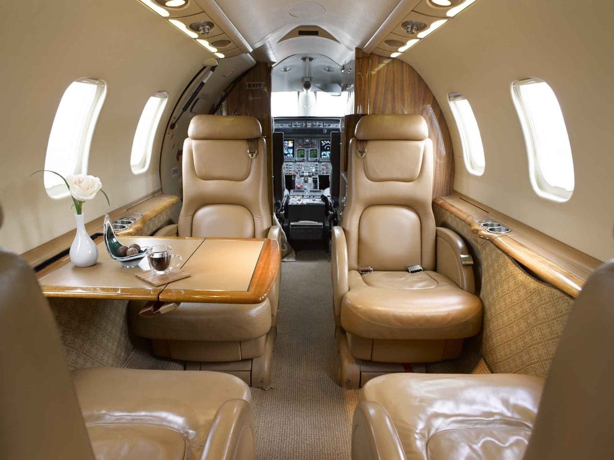 Interior view of the aircraft cabin with leather seats, a table, and a view towards the cockpit.