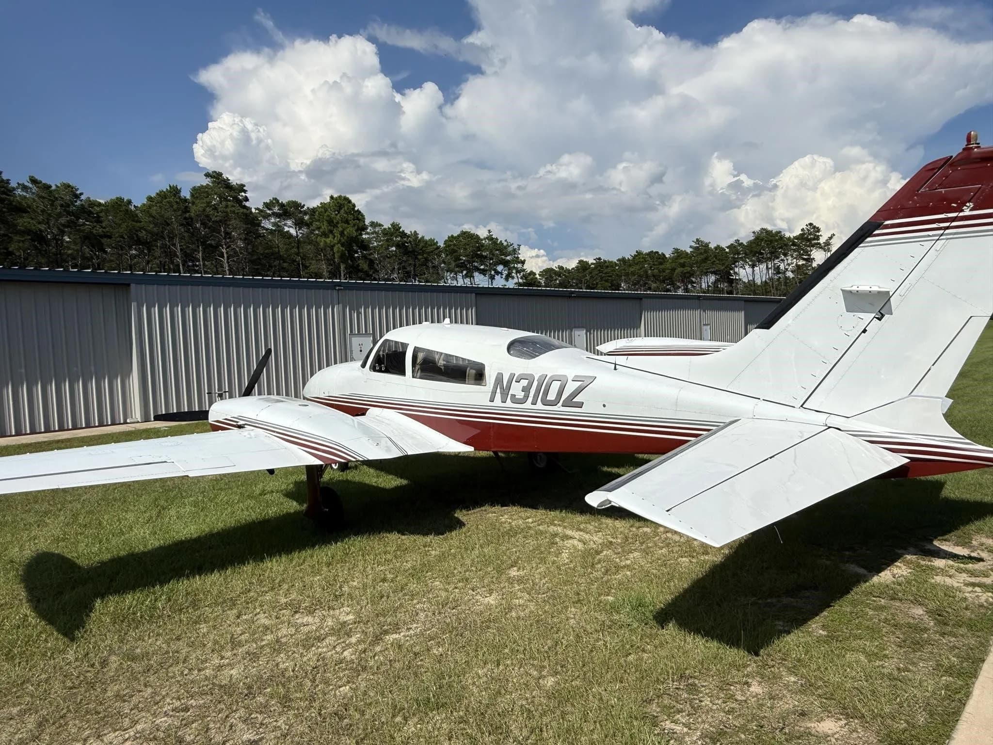 Rear-left view of a white and red twin-engine aircraft (N310Z) parked on grass next to a hangar.