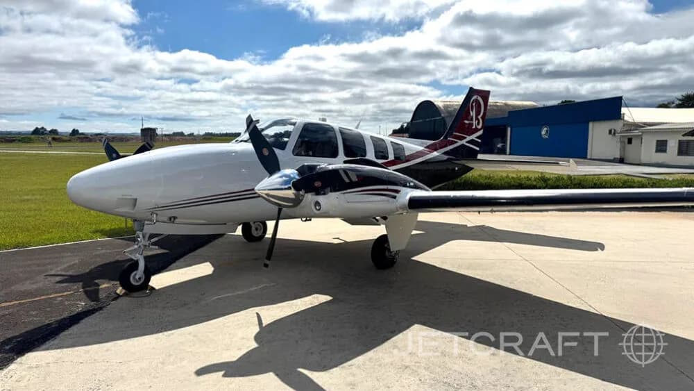 A white and black twin-engine propeller aircraft with red accents on the tail, parked on an asphalt ramp under a partly cloudy sky.