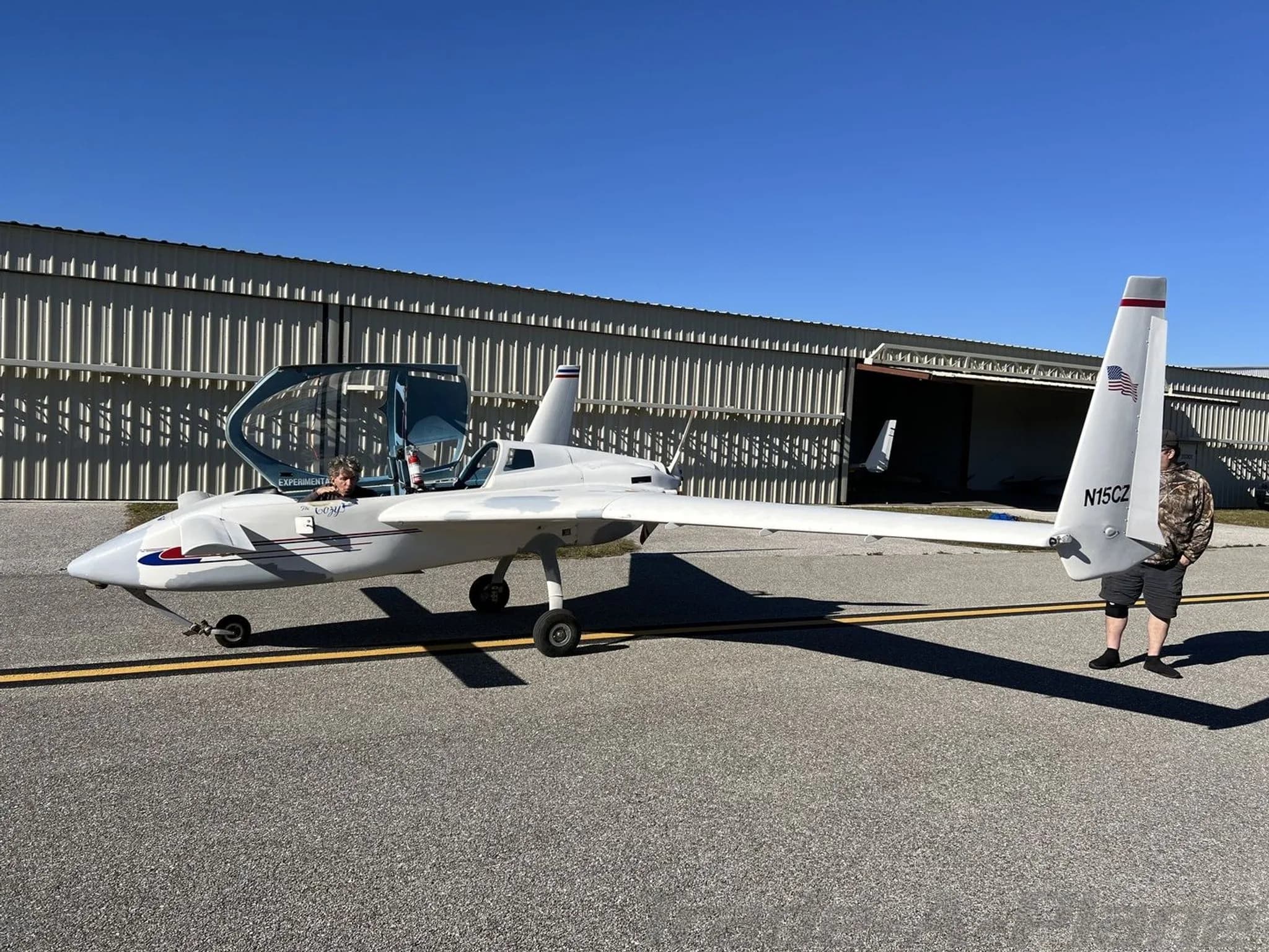 A white experimental aircraft with an open canopy and tail number N15CZ is parked on an airfield with two people nearby.