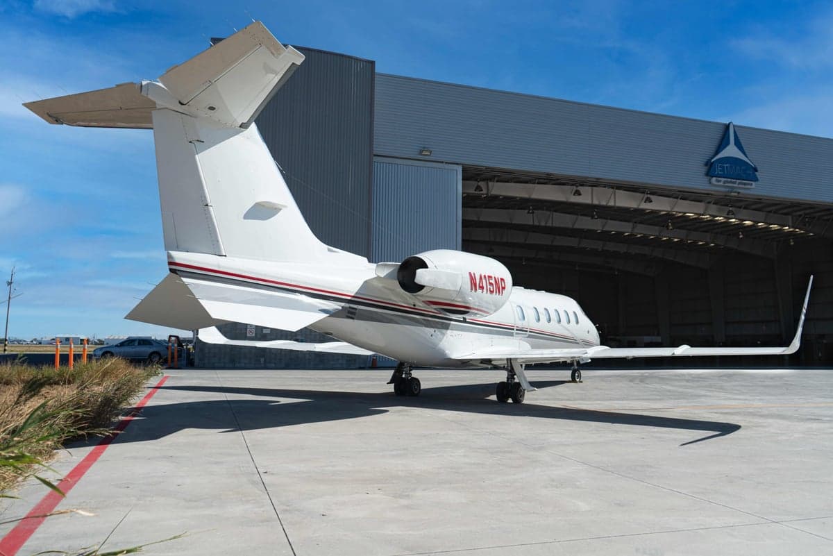 The rear of a white Learjet 45XR with registration N415NP is parked outside a hangar.