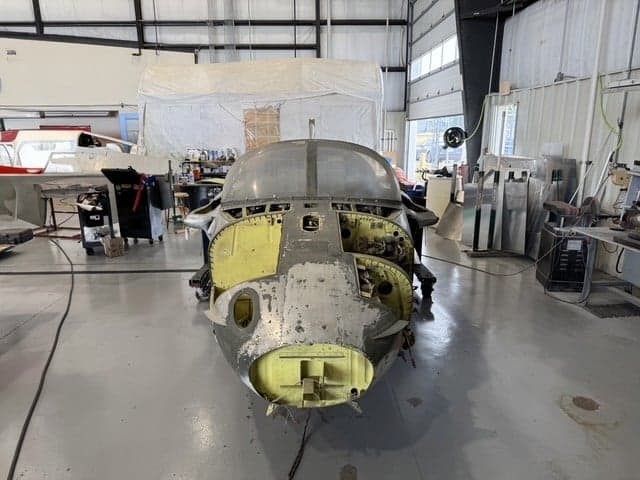 The front section of an aircraft undergoing restoration in a hangar.