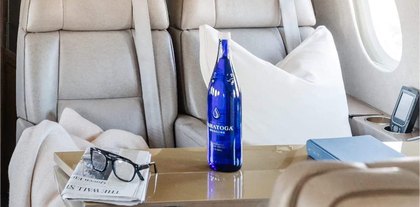 View of the aircraft's interior with light gray leather seats and a table with a bottle of water.