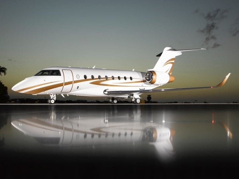 A white and gold aircraft is parked on a reflective surface at dusk.