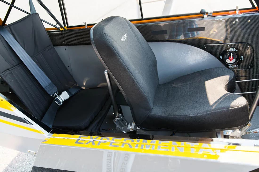 The interior of a Carbon Cub aircraft shows two black fabric seats and carbon fiber paneling.