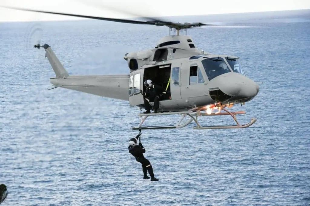 Bell UH-1 Iroquois helicopter with people rappelling from it.