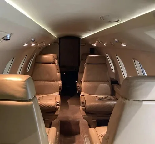 The interior cabin of a business jet with tan leather seats arranged in a club configuration.