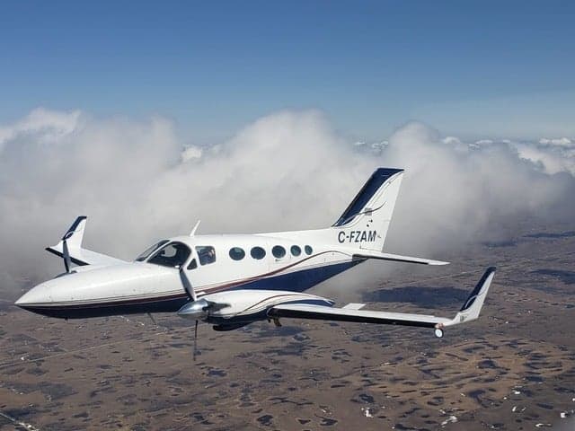 A white and blue twin-engine aircraft is flying in the sky.