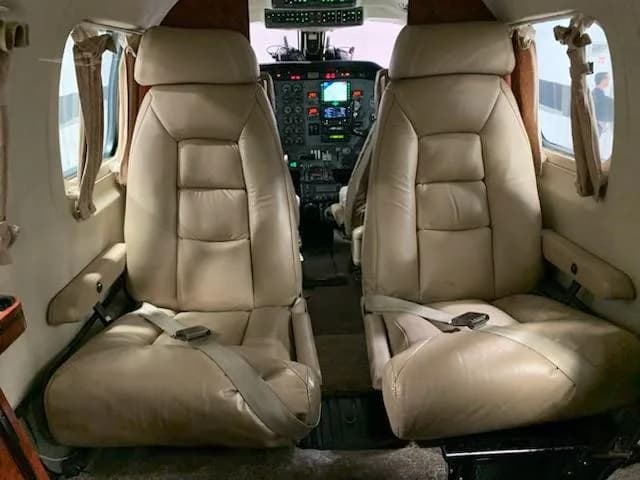 Two tan leather pilot and co-pilot seats are visible in the aircraft cabin, looking forward towards the cockpit.